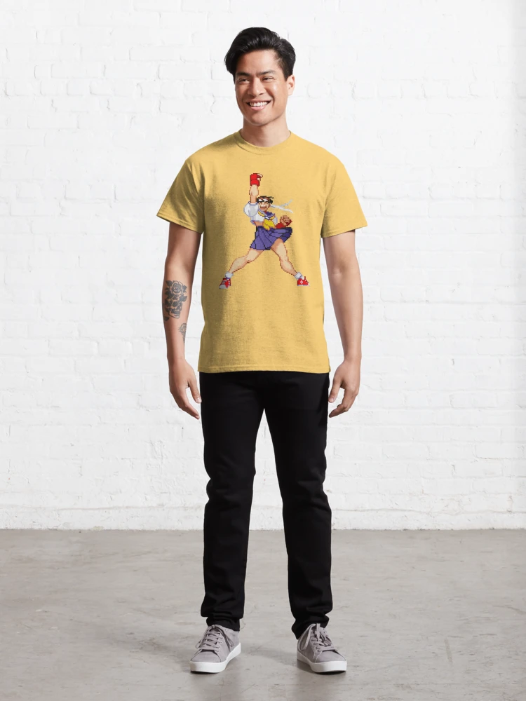 Homme qui porte un tee-shirt jaune clair Street Fighter avec le personnage Sakura qui lève le poing